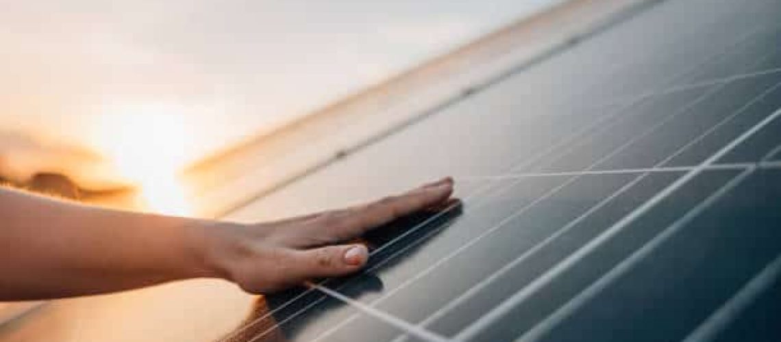 Close-up of human hand touching solar panel during Sunset